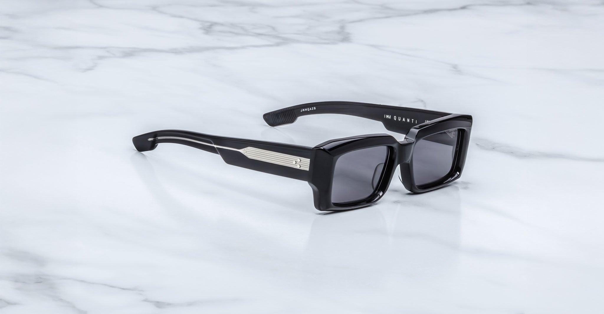 Jacques Marie Mage Quant in Shadow, rectangular black acetate sunglasses shown from a side angle, featuring bold sculpted rims, wide temples with signature metal inlay, and dark tinted lenses on a light marble surface.