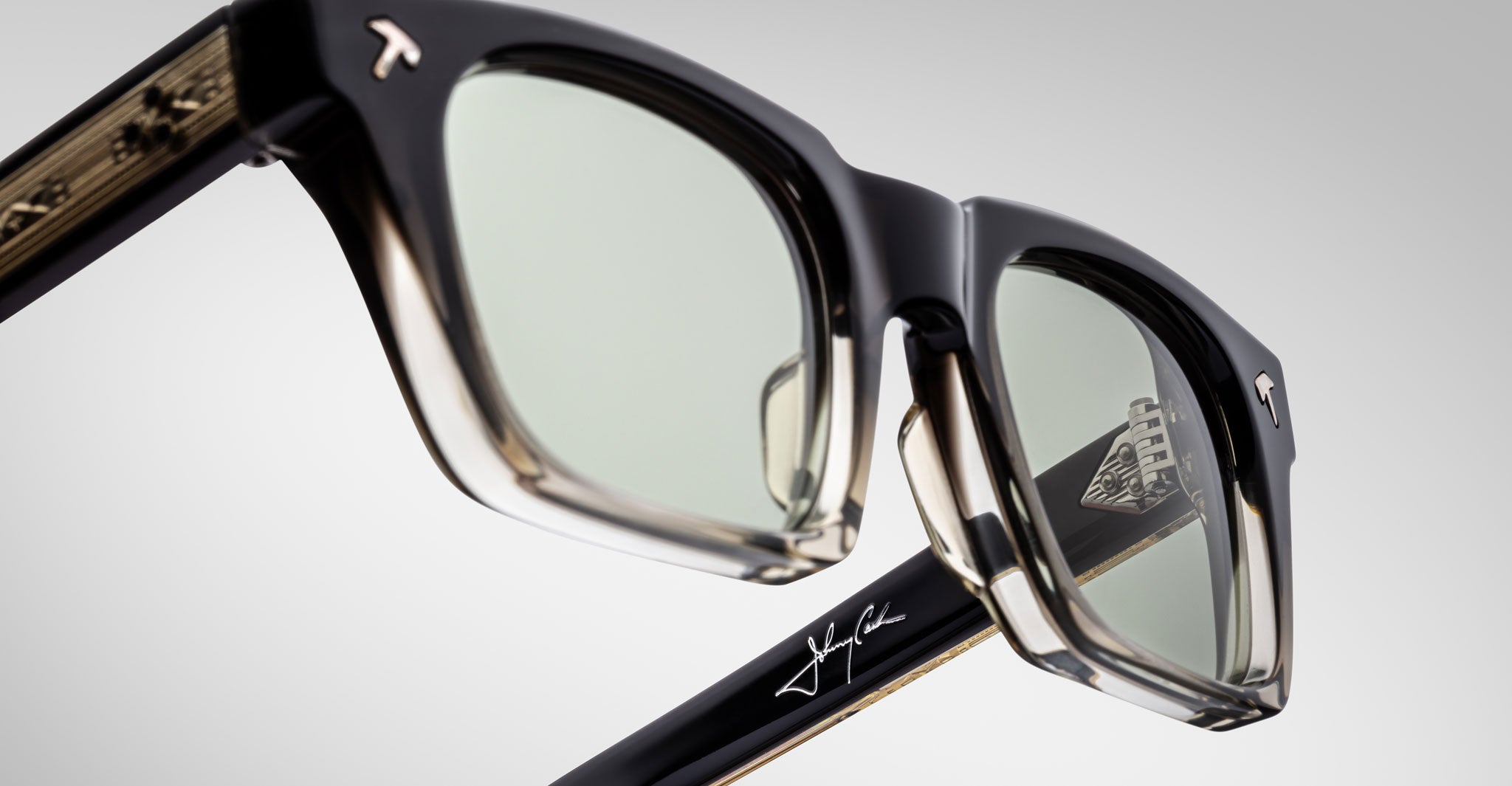 Close-up view of Jacques Marie Mage Quentin sunglasses with green lenses, T logos, and signature visible on frame and temple.