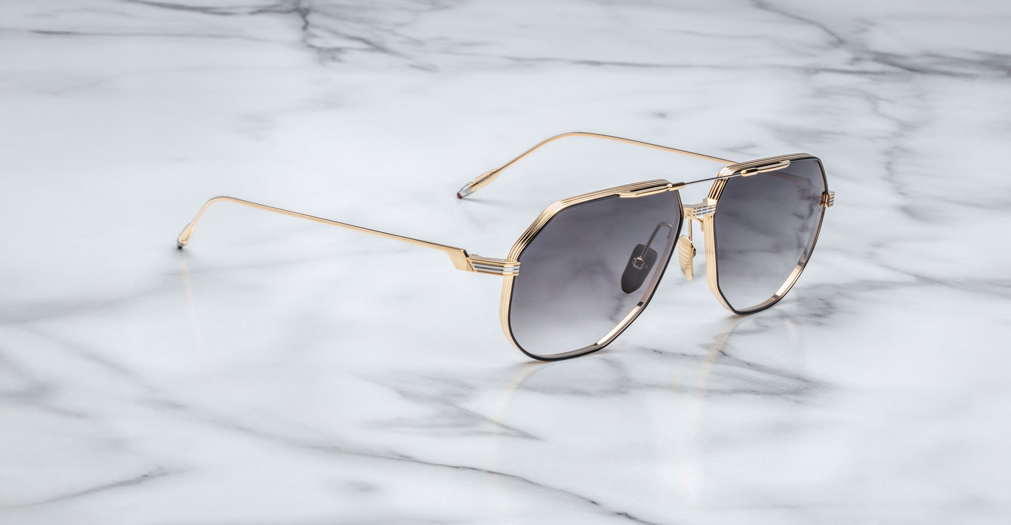 Jacques Marie Mage Reynold gold-framed oversized aviator sunglasses with dark tinted lenses are displayed on white marble, highlighting their classic 70s-inspired style.