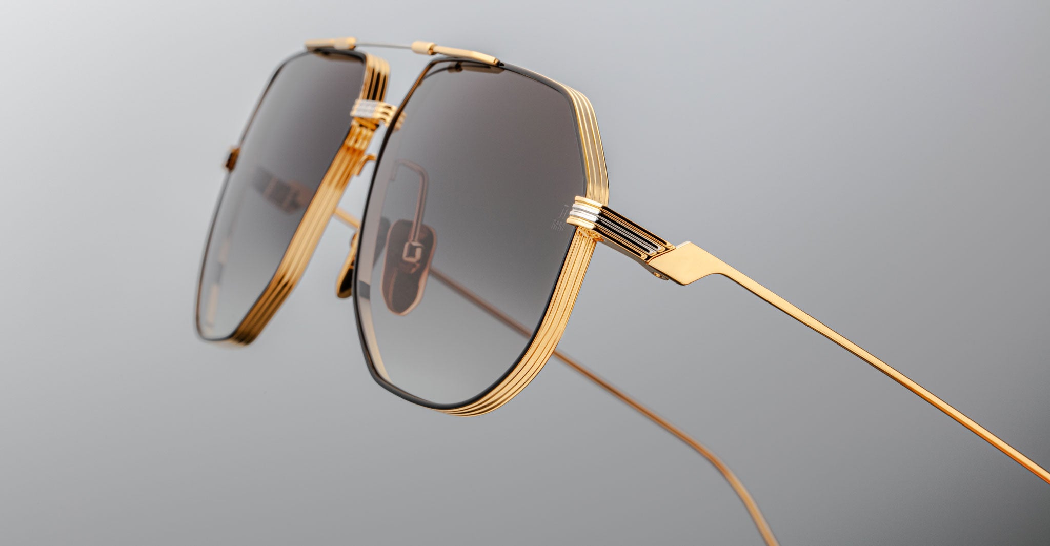 Close-up of Jacques Marie Mage Reynold oversized aviator sunglasses with a gold titanium frame and dark tinted lenses, inspired by 70s eyewear. Frame details and a sleek design stand out against a light gray background.