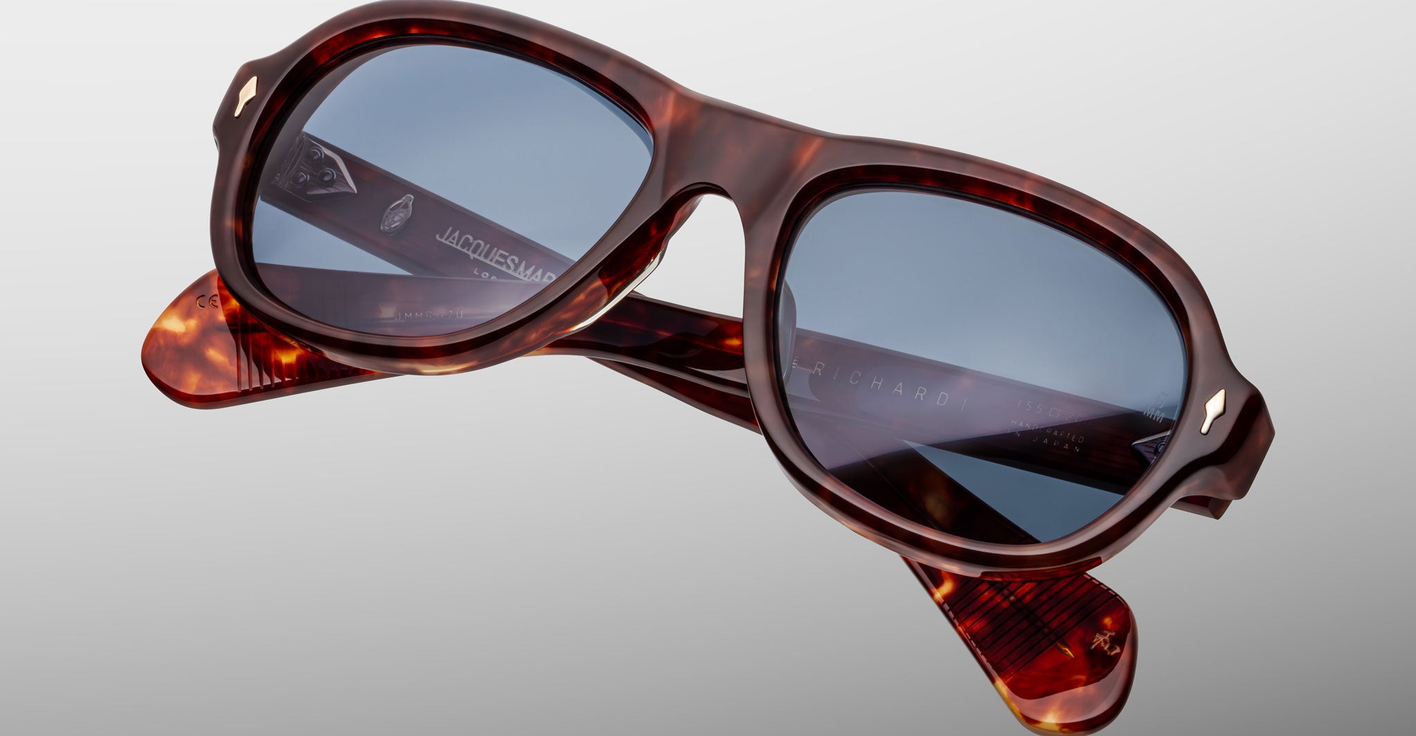 Close-up of Jacques Marie Mage Richard tortoiseshell sunglasses with blue-tinted lenses, folded against a plain light gray background.