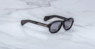 Jacques Marie Mage Richard black sunglasses with dark lenses and thick frames rest on a white marble surface, with the brand name visible on the inside of one temple arm.