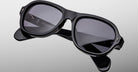 The Jacques Marie Mage Richard sunglasses feature thick, glossy black frames with dark lenses and visible brand markings on the arms, displayed against a light gray background.