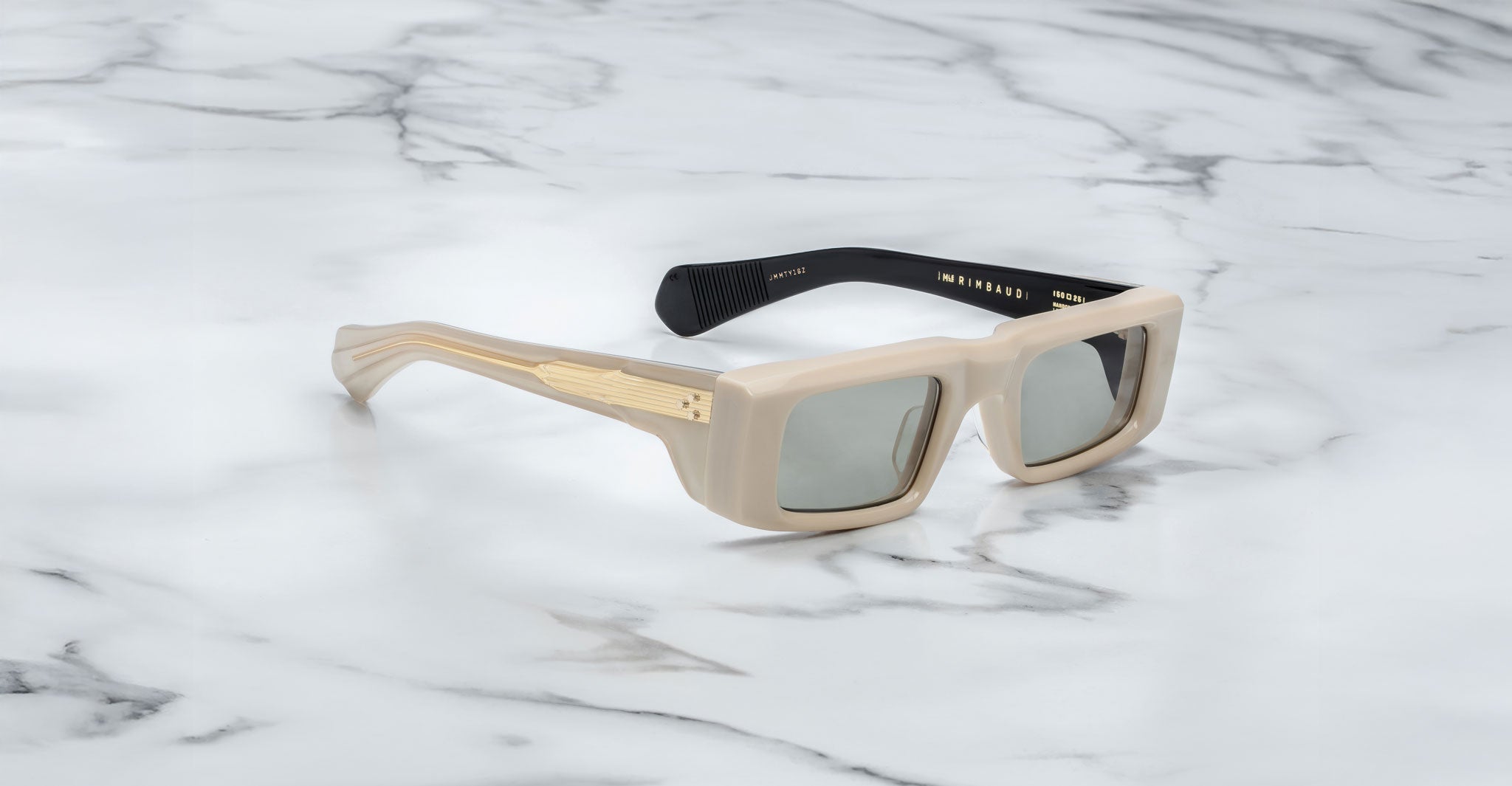 Profile view of the Jacques Marie Mage Rimbaud sunglass in cream color with light grey lenses on a white marbled with grey veining background