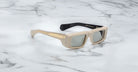 Profile view of the Jacques Marie Mage Rimbaud sunglass in cream color with light grey lenses on a white marbled with grey veining background