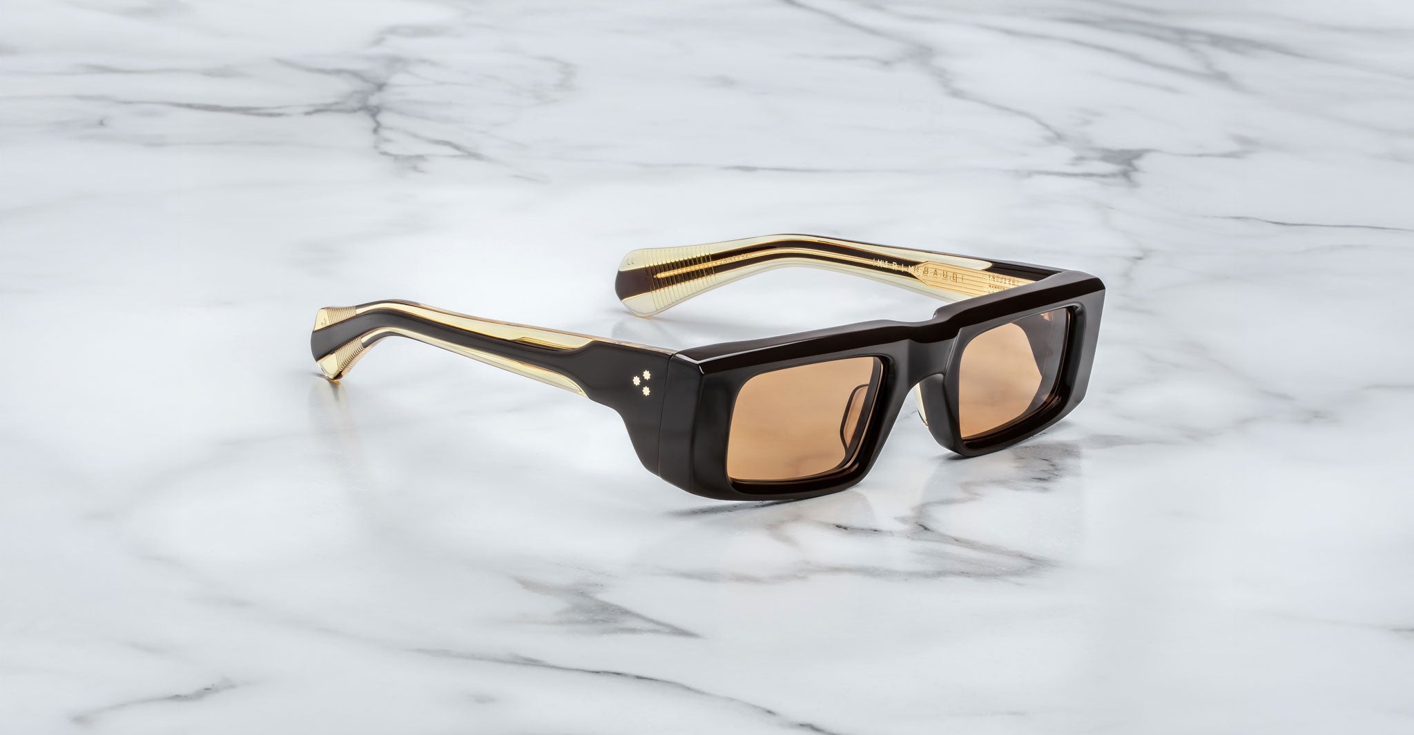 Profile view of the Jacques Marie Mage Rimbaud sunglass in walnut color with orange lenses on a white marbled with grey veining background