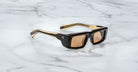 Profile view of the Jacques Marie Mage Rimbaud sunglass in walnut color with orange lenses on a white marbled with grey veining background