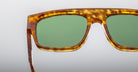 Close-up of the upper half of Jacques Marie Mage Ritz sunglasses featuring green lenses and a thick, mottled brown tortoiseshell frame against a plain light background.