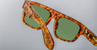 Close-up view of Jacques Marie Mage Ritz tortoiseshell sunglasses with green lenses, one arm extended and the other partially visible, set against a plain light gray background.