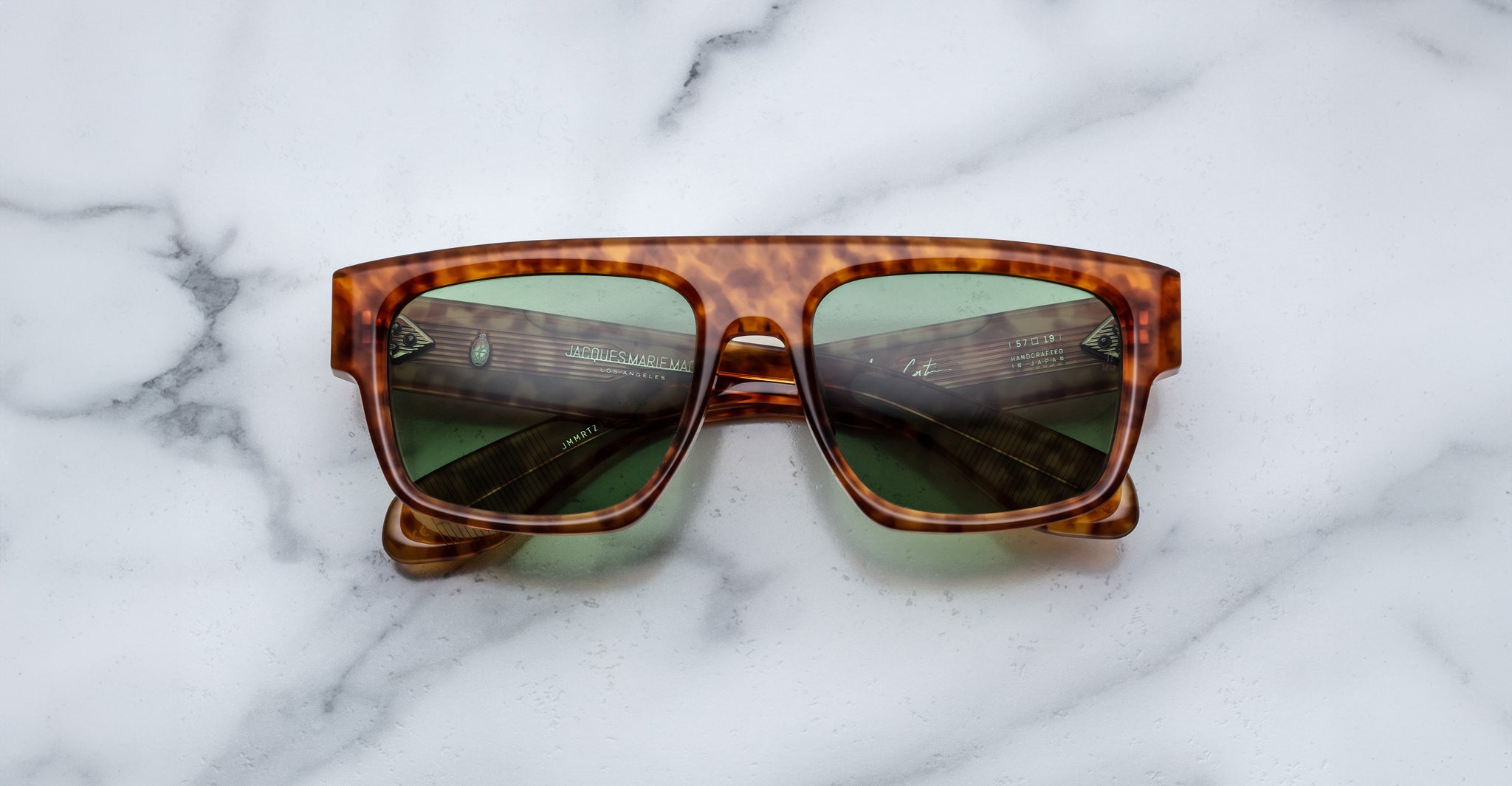 The Jacques Marie Mage Ritz rectangular tortoiseshell sunglasses with green lenses rest on a white marble surface.