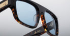 Close-up of Jacques Marie Mage Ritz tortoiseshell eyeglasses with blue-tinted lenses, gold detailing on the arms, and a signature reading by Cut on the inner side of one arm.