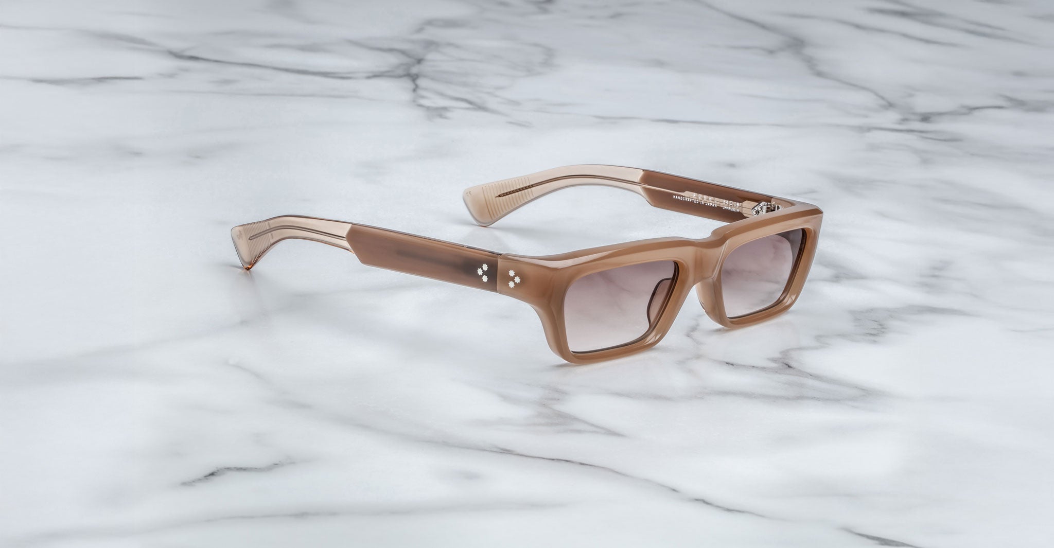 The Jacques Marie Mage Rush, a pair of square brown sunglasses with thick frames and gradient lenses, rests on a white marble surface.