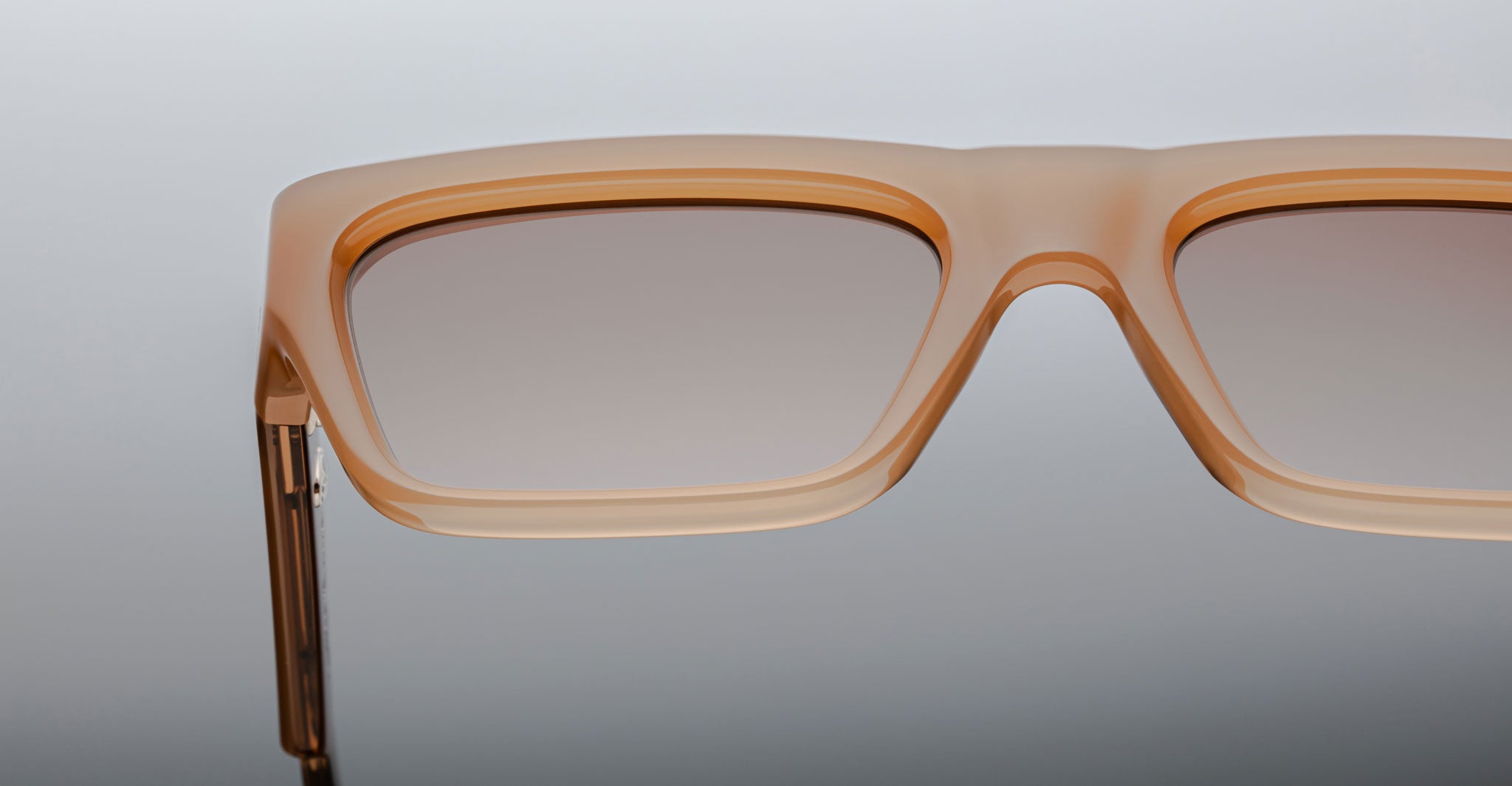 Close-up of the top half of Jacques Marie Mage Rush rectangular sunglasses, featuring light brown translucent frames and gradient tinted lenses, set against a neutral background.