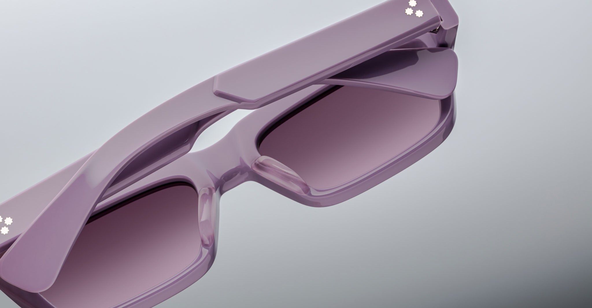 A close-up photo of Jacques Marie Mage Rush rectangular sunglasses with thick, glossy lavender frames and matching tinted lenses, displayed on a light grey surface.
