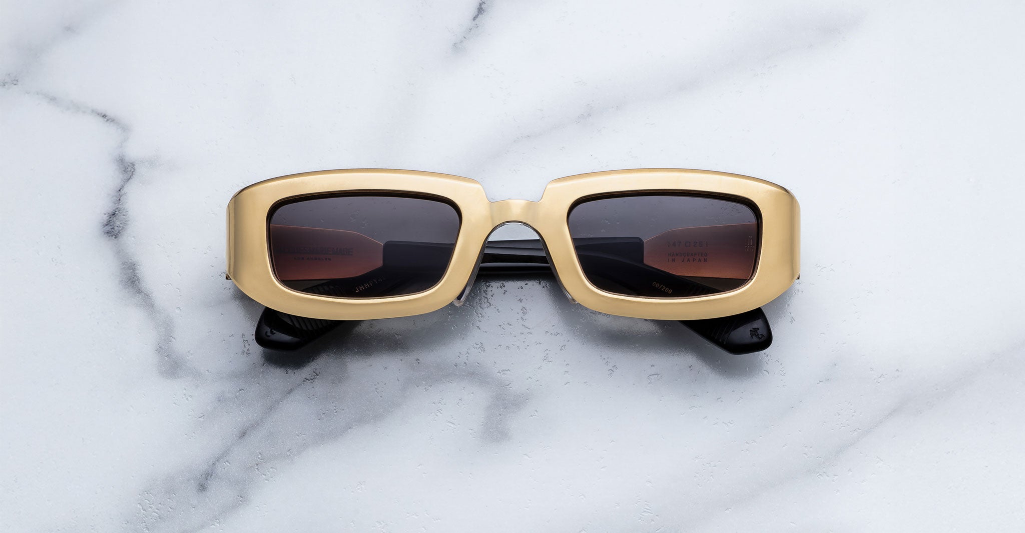 Jacques Marie Mage Ryder in Gold, rectangular gold-tone acetate sunglasses with thick sculpted rims, a low-profile bridge, and gradient tinted lenses, shown front-facing on a light marble surface.