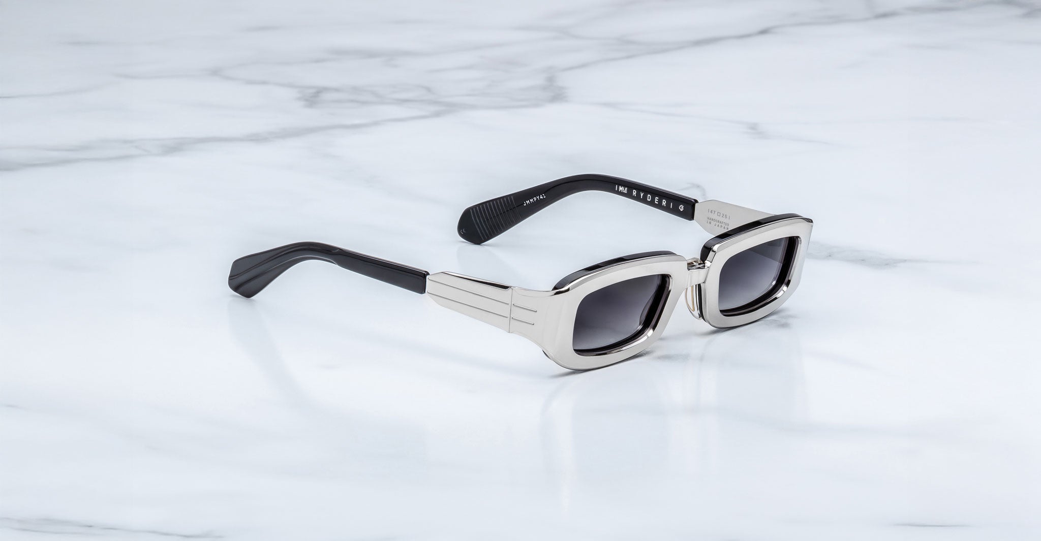 Jacques Marie Mage Ryder in Silver, rectangular silver-tone acetate sunglasses shown from a side angle, featuring thick sculpted rims, wide temples with stepped detailing, and gradient tinted lenses on a light marble surface.