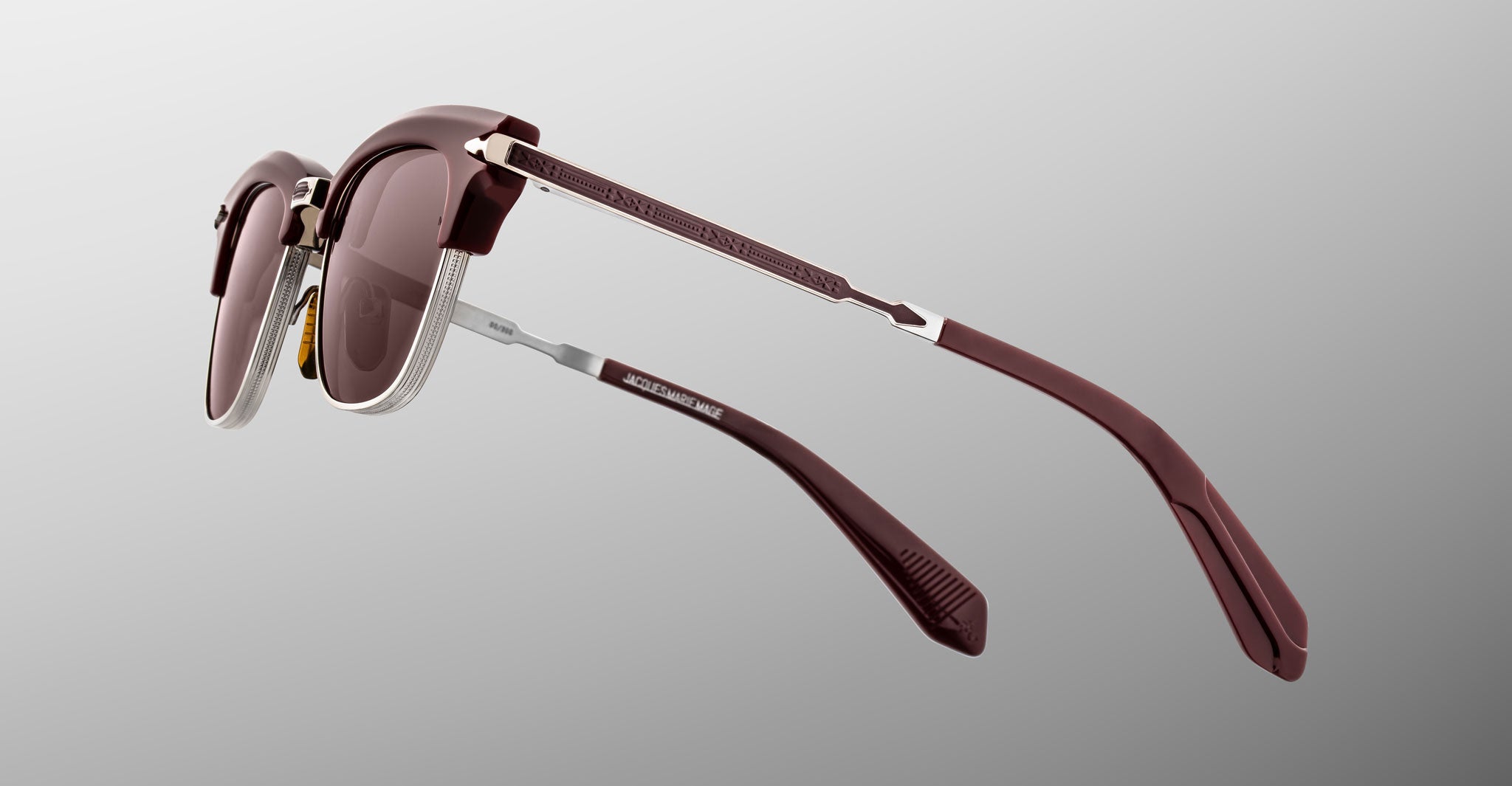 The Jacques Marie Mage Sartre sunglasses by Jacques Marie Mage feature maroon frames with silver accents and brown-tinted lenses, inspired by 50s clubmaster style, shown from the back and side against a gray gradient background.