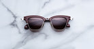 Jacques Marie Mage Sartre sunglasses in brown and silver with dark lenses rest on a white marble surface.