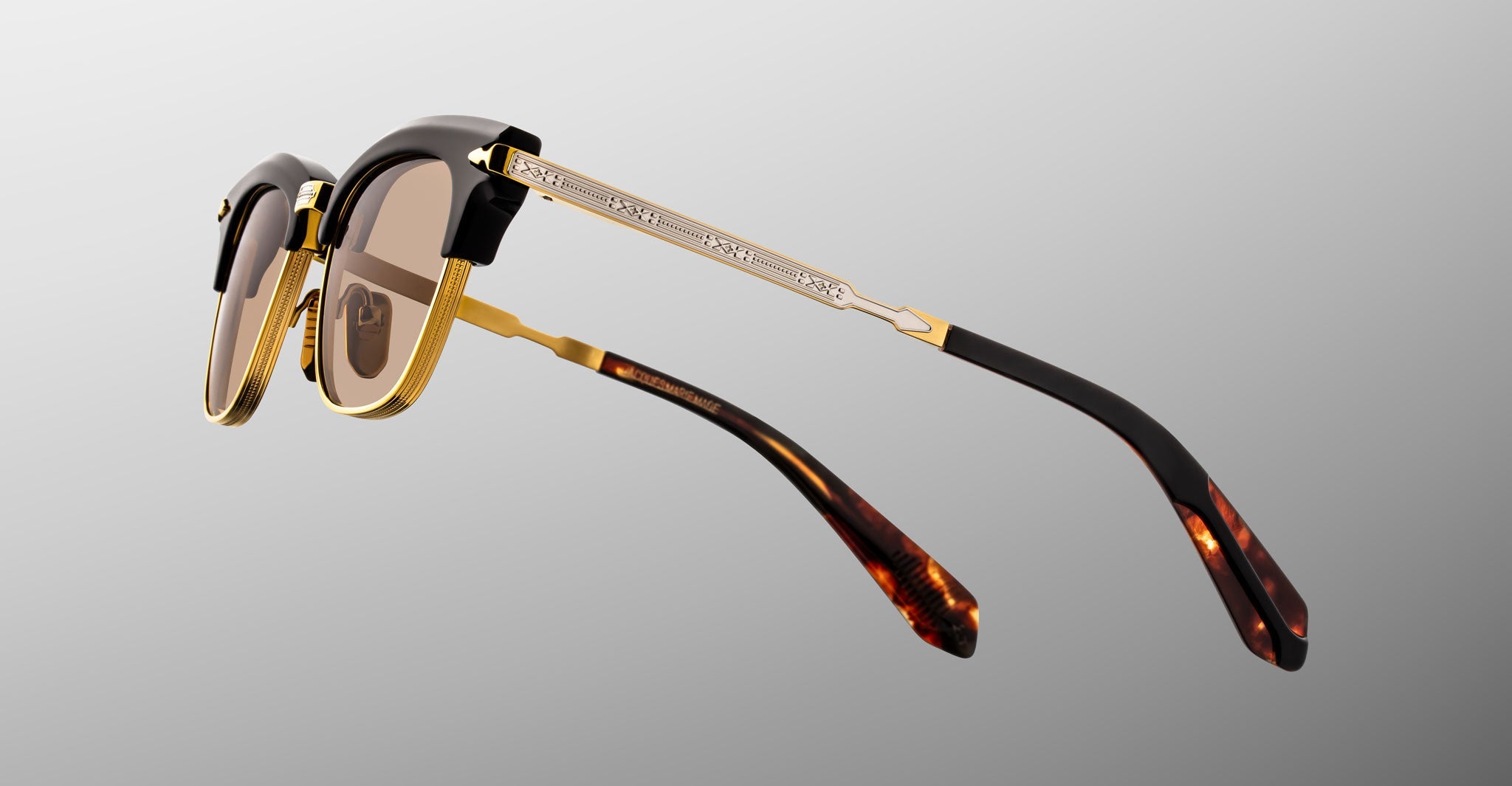 A pair of Jacques Marie Mage Sartre glasses with gold rims, brown tinted lenses, and tortoiseshell-patterned arms displayed against a gray background.