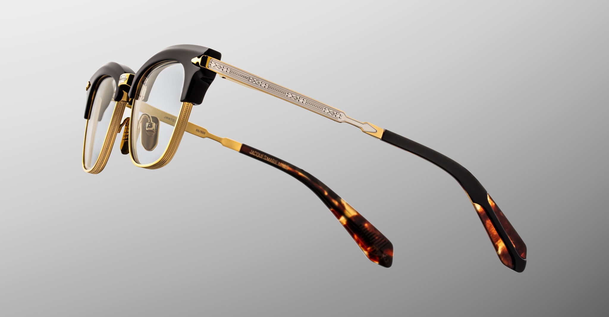 The Jacques Marie Mage Sartre glasses feature gold metal frames, black accents on the browline and temples, and tortoiseshell-patterned temple tips, shown against a neutral background.