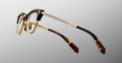 The Jacques Marie Mage Sartre glasses feature gold metal frames, black accents on the browline and temples, and tortoiseshell-patterned temple tips, shown against a neutral background.
