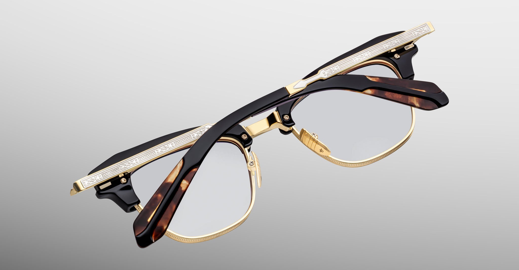 The Jacques Marie Mage Sartre glasses feature gold detailing, tortoiseshell-patterned arms, and clear lenses in a classic clubmaster frame by Jacques Marie Mage, shown against a light gray background.