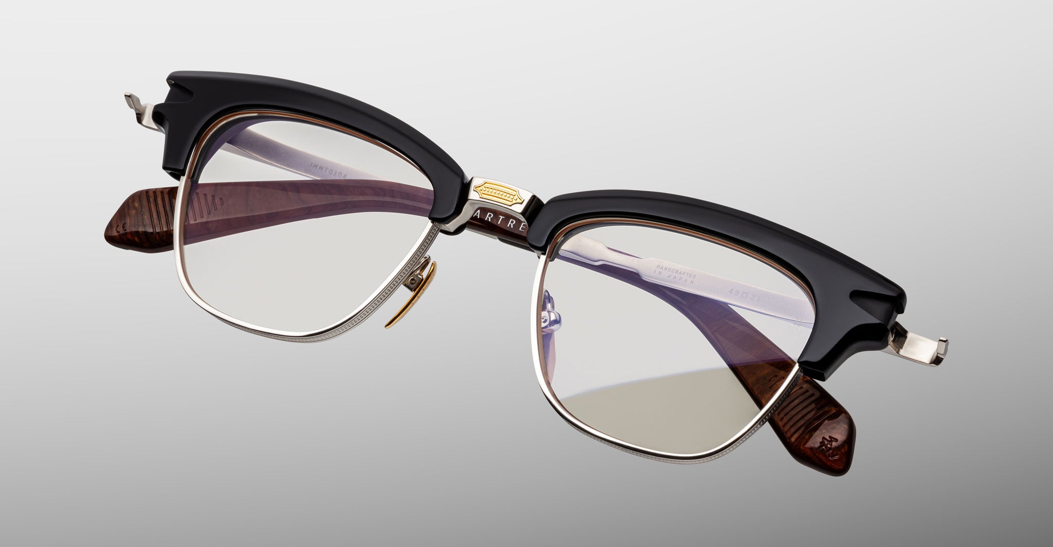 The Jacques Marie Mage Sartre by Jacques Marie Mage is a vintage-style clubmaster frame featuring black upper rims, silver metal frames, clear lenses, and brown temple arms for timeless appeal.