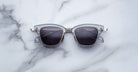 A pair of Jacques Marie Mage Sartre glasses with silver frames and dark lenses rests on a white marble surface.