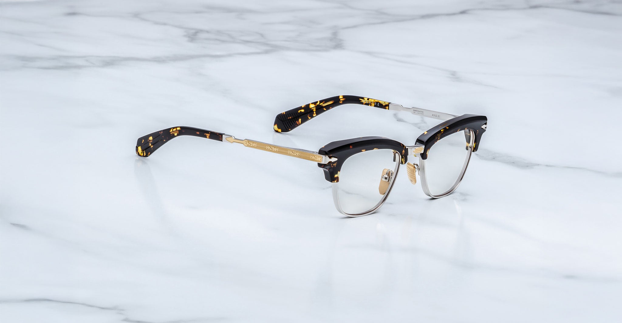 Jacques Marie Mage Sartre optical eyeglasses by Jacques Marie Mage, featuring gold metal rims and black tortoiseshell arms, are displayed on a white marble surface.