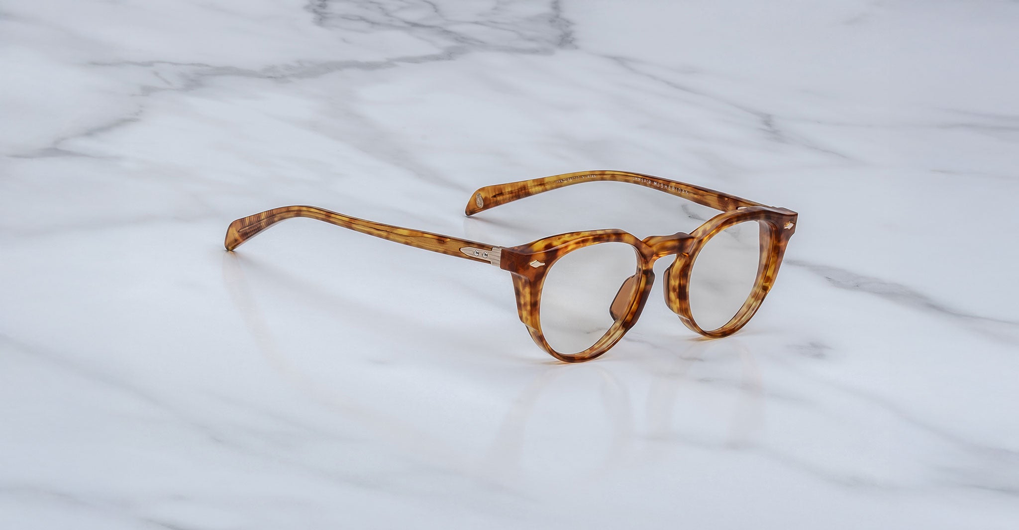 The Jacques Marie Mage Sheridan, round tortoiseshell eyeglasses with thick frames, rest on a white marble surface.