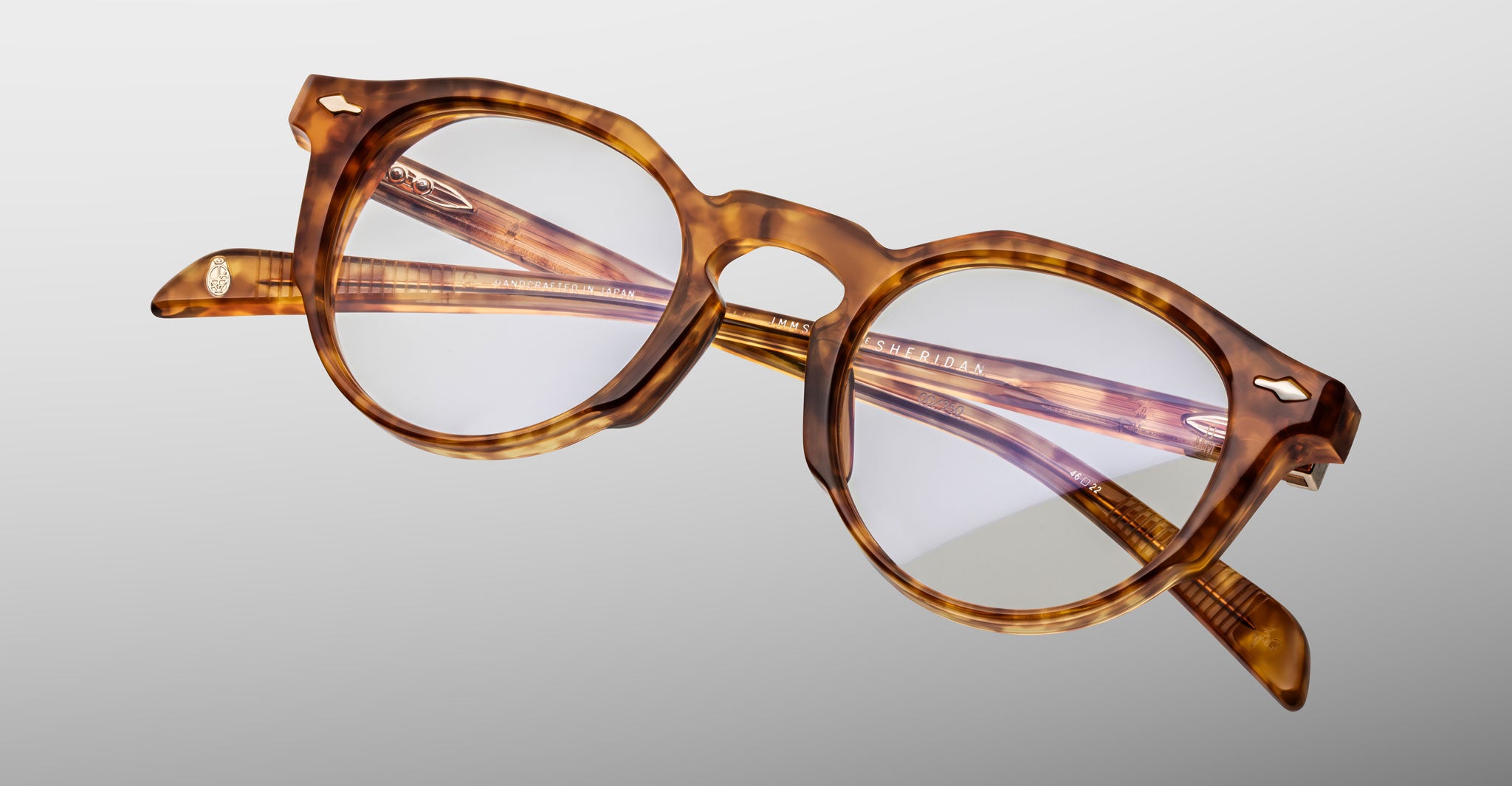 The Jacques Marie Mage Sheridan eyeglasses feature round, thick tortoiseshell frames with clear lenses, displayed against a plain light gray background.