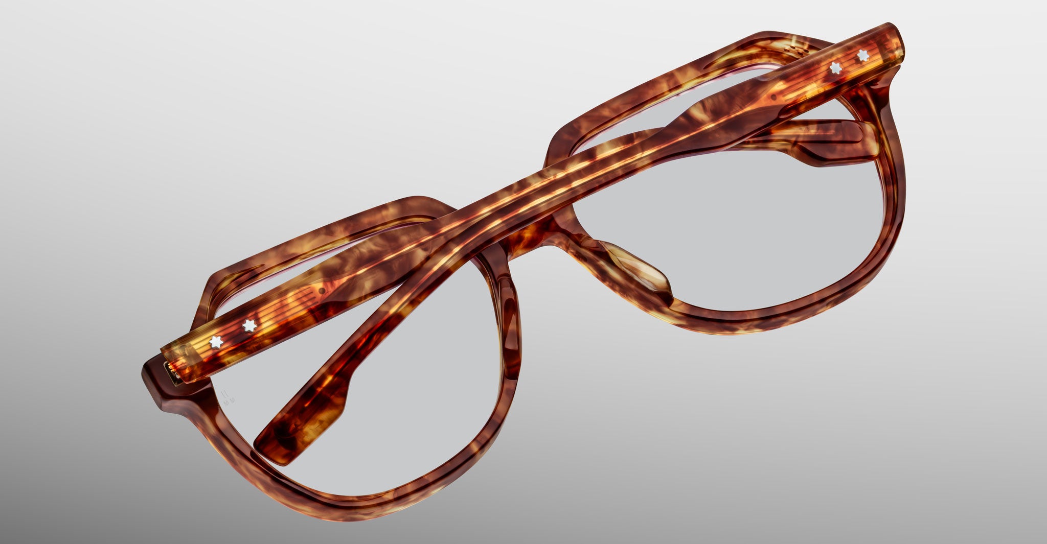 A pair of Jacques Marie Mage Shozo brown tortoiseshell eyeglasses with thick frames, folded upside down on a light gray background.