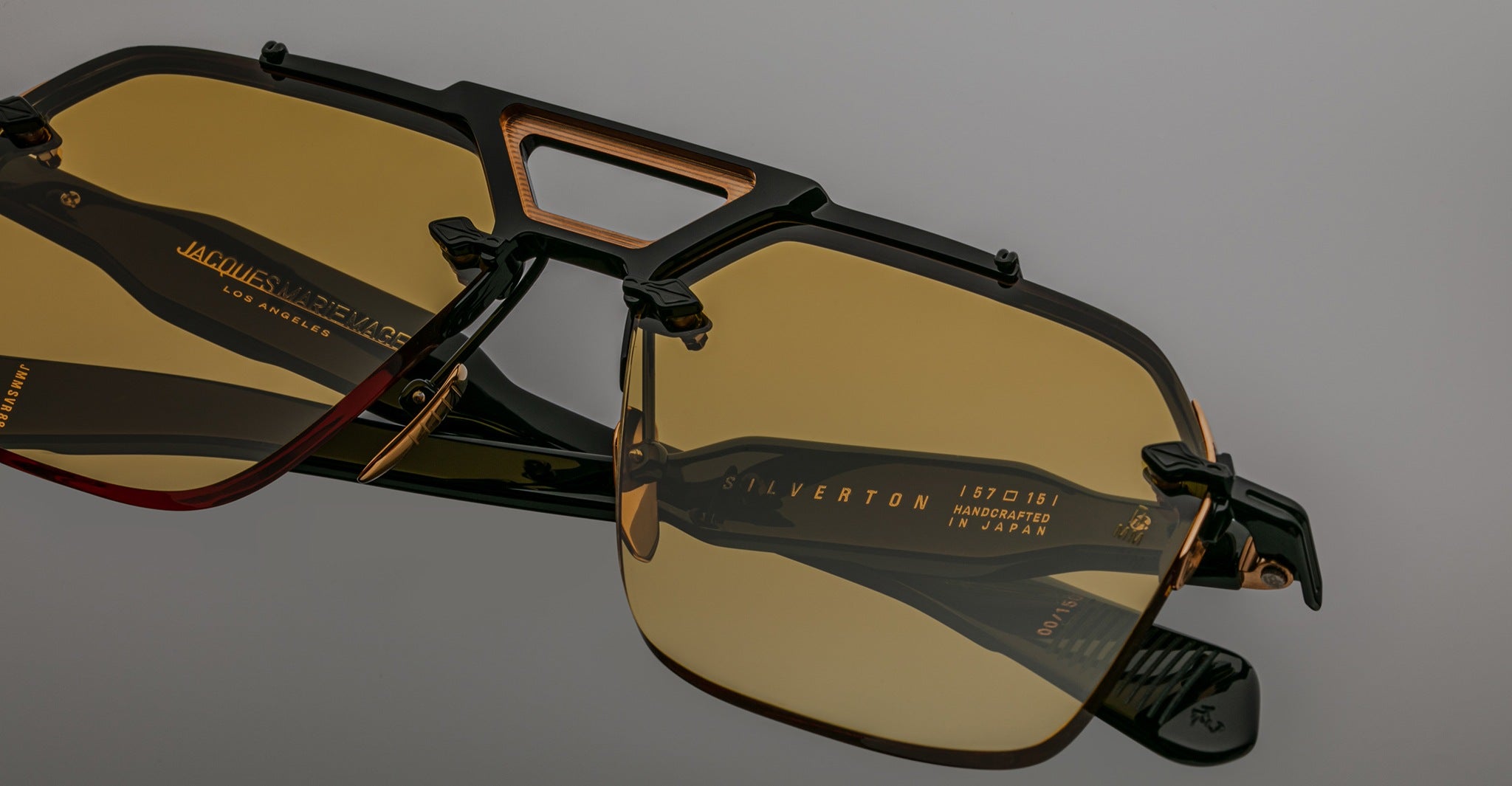 Close-up of Jacques Marie Mage Silverton rectangular sunglasses featuring yellow-tinted lenses and black-and-gold frames. Branding and SILVERTON are visible on one lens, with text showing they are made in Japan.