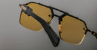 A close-up of the Jacques Marie Mage Silverton sunglasses featuring yellow-tinted lenses and black arms, set against a neutral gray background with focus on the side and front frames.