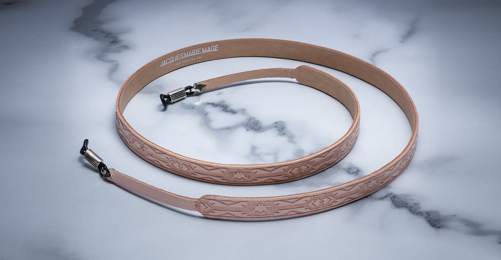 Jacques Marie Mage Strap Tooled tan leather guitar strap with engraved patterns, top view. No sunglasses or eyeglasses shown.