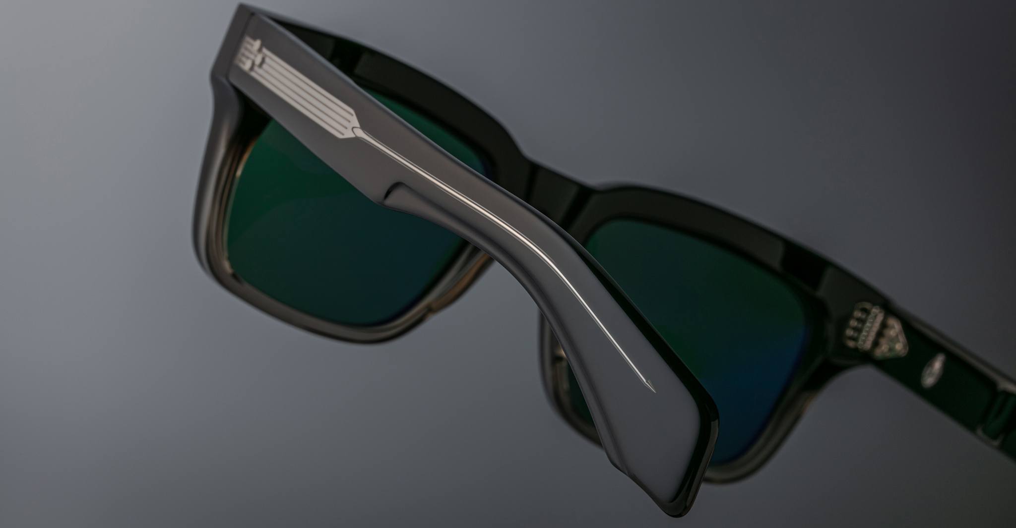 Close-up of Jacques Marie Mage Torino rectangular eyeglass frames in black, featuring green-tinted lenses, handcrafted acetate construction, detailed side arms, and a small logo on the lens.