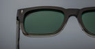 Close-up of the Jacques Marie Mage Torino sunglasses by Jacques Marie Mage, featuring bold rectangular black handcrafted acetate frames with dark green lenses against a plain background.