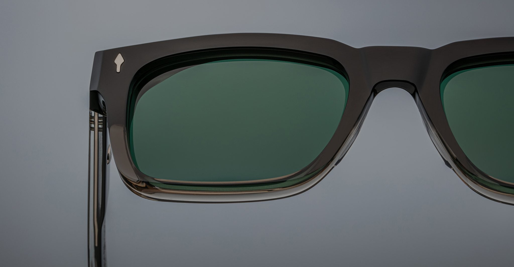 Close-up of the Jacques Marie Mage Torino sunglasses by Jacques Marie Mage, featuring bold rectangular black handcrafted acetate frames with dark green lenses against a plain background.