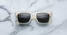 Jacques Marie Mage Torino eyeglasses by Jacques Marie Mage feature bold clear rectangular frames with dark lenses, displayed on a white marble surface.