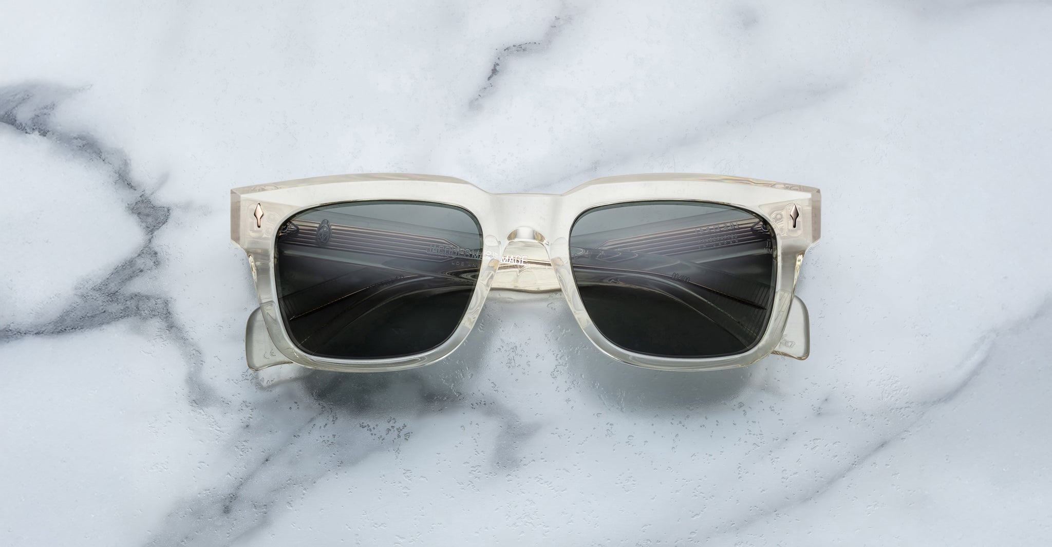 Jacques Marie Mage Torino eyeglasses by Jacques Marie Mage feature bold clear rectangular frames with dark lenses, displayed on a white marble surface.
