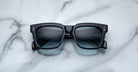 The Jacques Marie Mage Torino by Jacques Marie Mage are black rectangular sunglasses with dark tinted lenses and bold frames, displayed on a white marble surface.