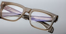 Close-up of Jacques Marie Mage Torino eyeglasses, bold rectangular frames in handcrafted acetate with clear lenses, reflective details, and Jacques Marie Mage branding on the temples.