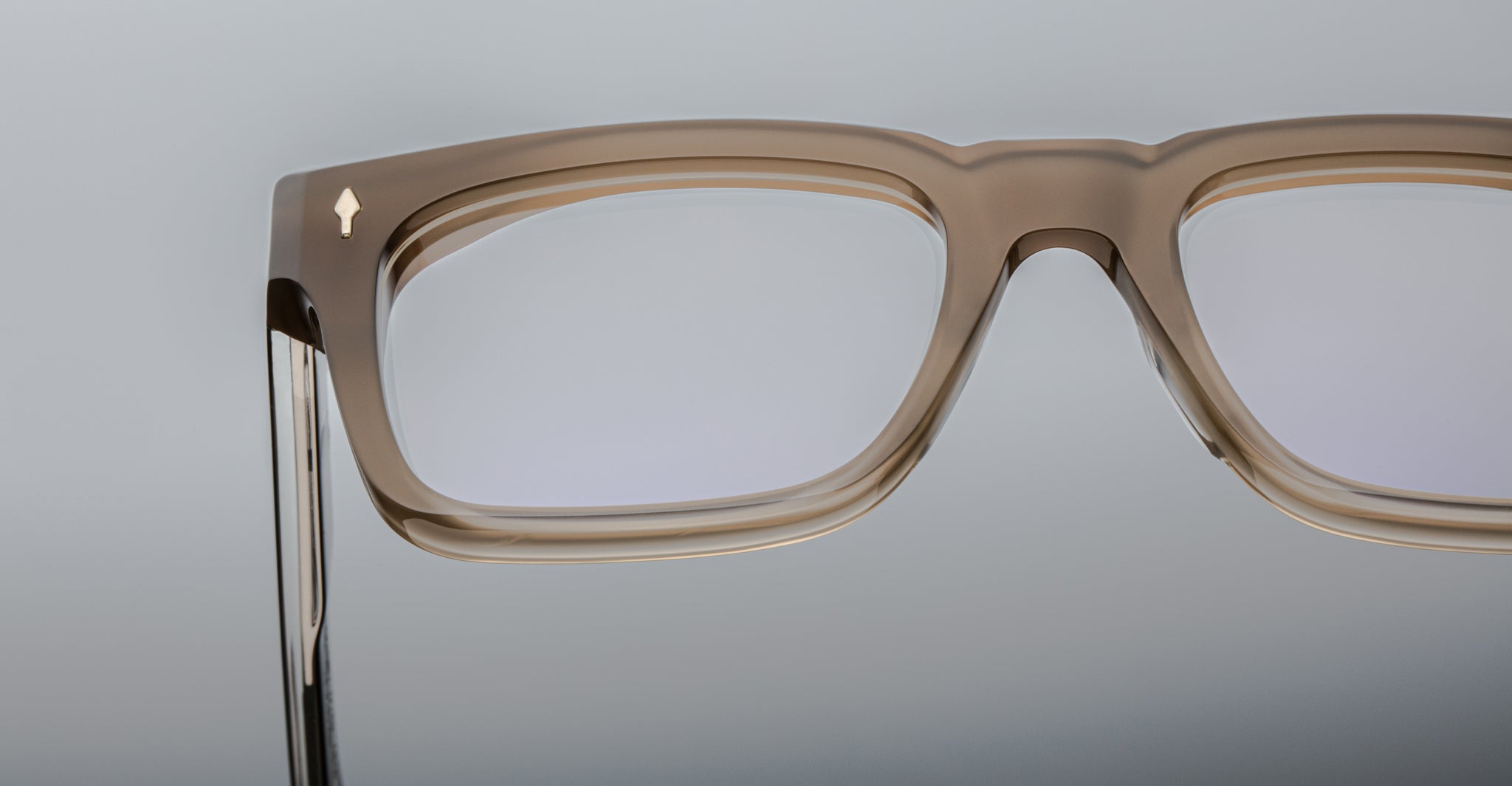 Close-up of the upper section of rectangular Jacques Marie Mage Torino eyeglass frames, featuring handcrafted translucent brown acetate, set against a plain light background.