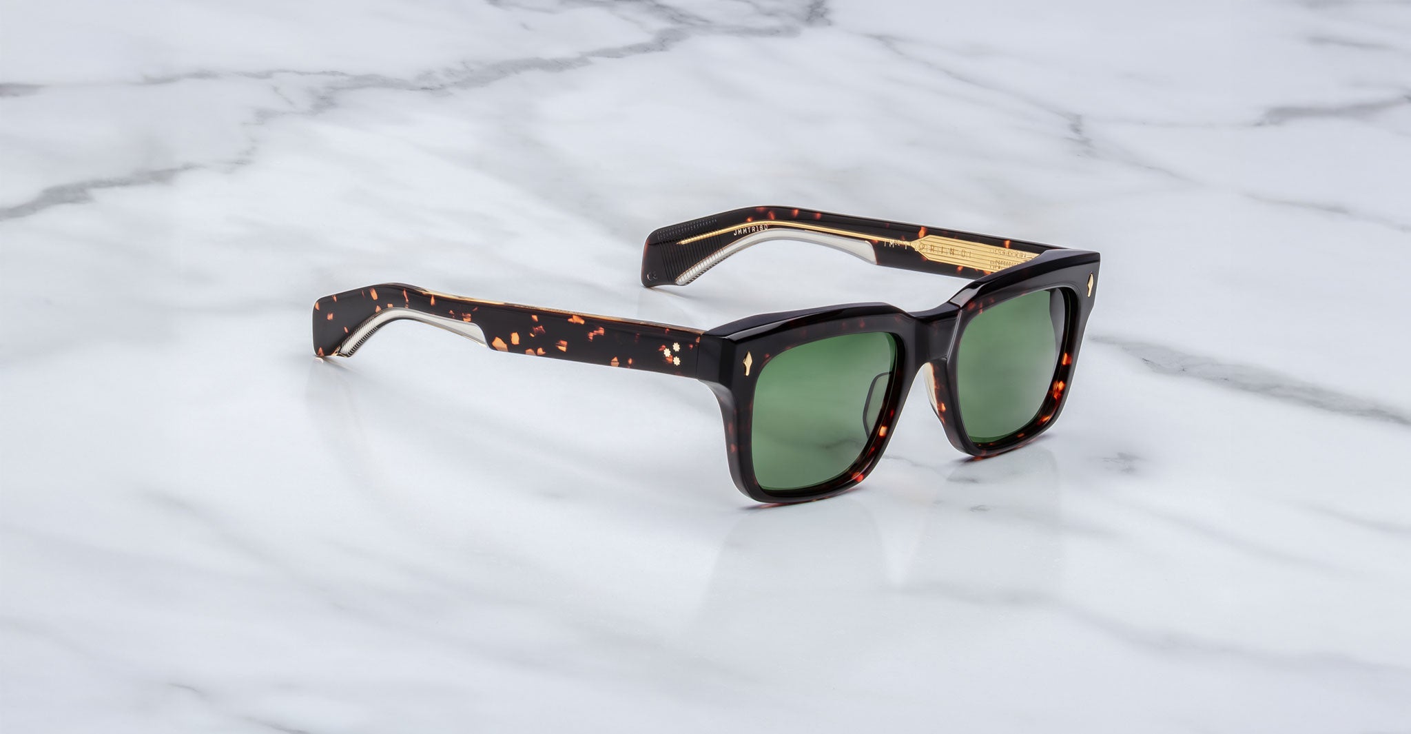Jacques Marie Mage Torino sunglasses by Jacques Marie Mage feature bold rectangular tortoiseshell frames and green lenses, reminiscent of handcrafted acetate eyewear, displayed on a white marble surface.