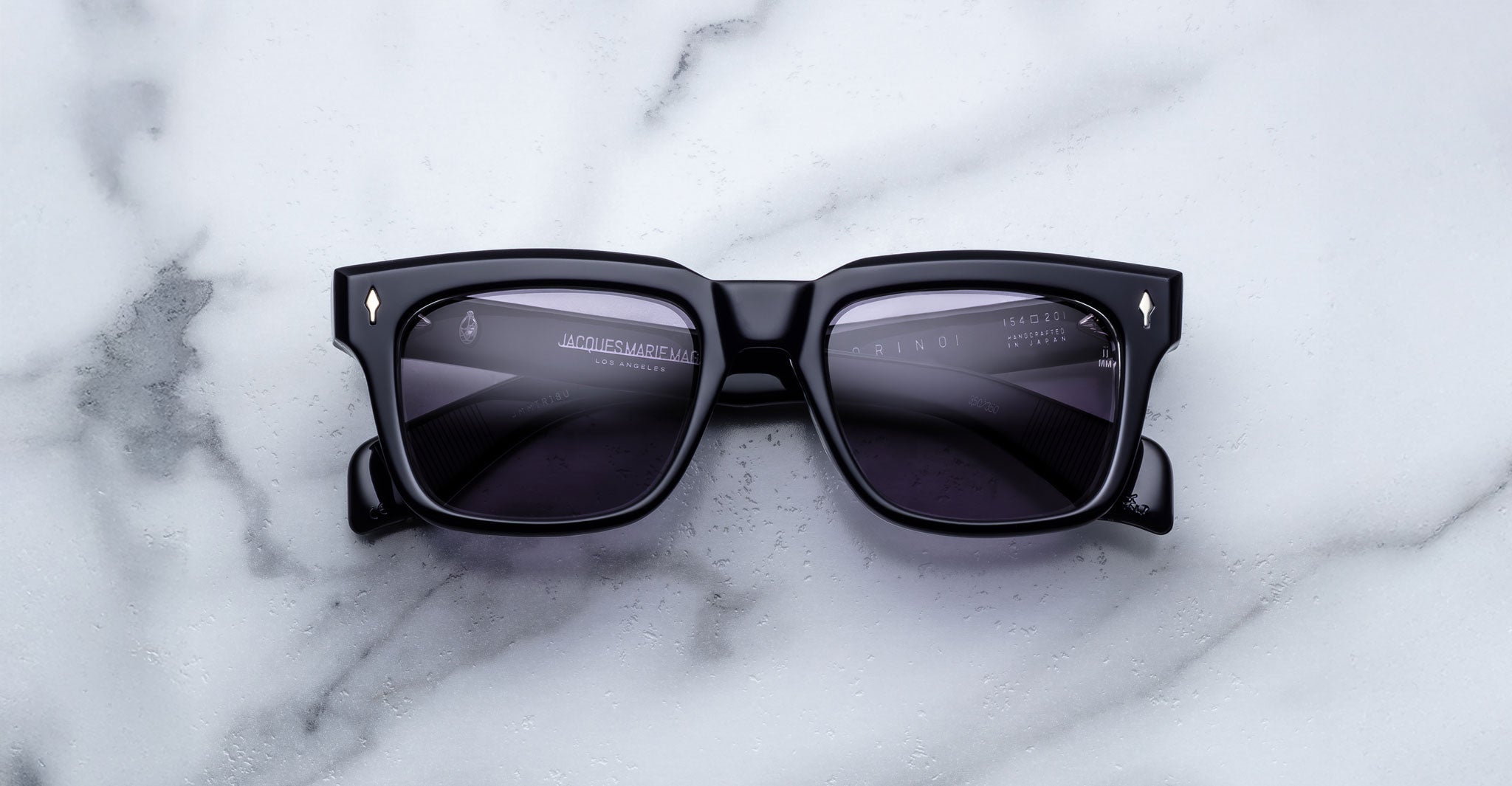 Jacques Marie Mage Torino black rectangular sunglasses with dark lenses and bold frames by Jacques Marie Mage, displayed on a white marble surface.