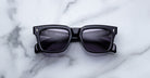 Jacques Marie Mage Torino black rectangular sunglasses with dark lenses and bold frames by Jacques Marie Mage, displayed on a white marble surface.