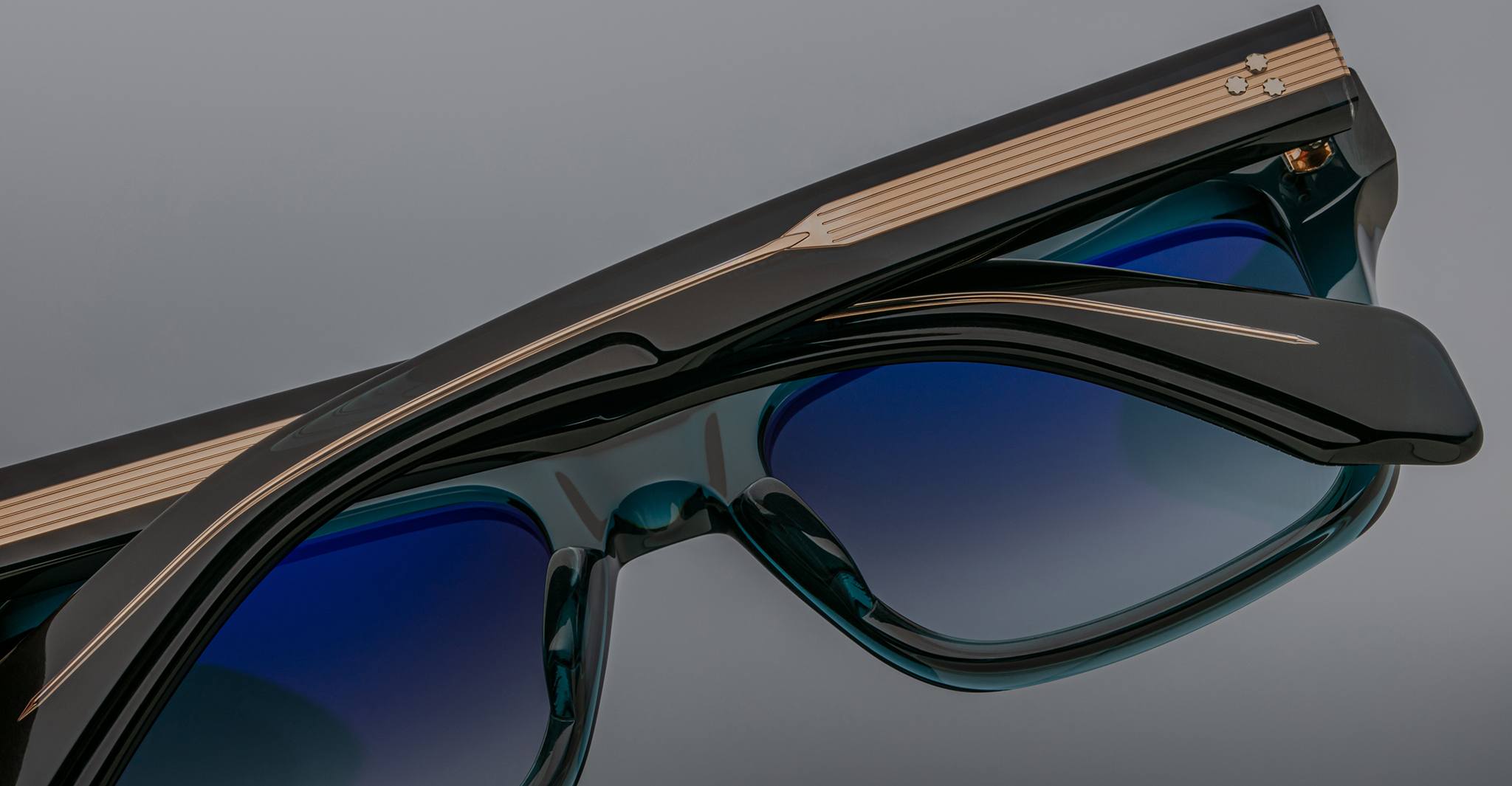 Close-up of two pairs of Jacques Marie Mage Torino sunglasses by Jacques Marie Mage, featuring bold rectangular frames with gold detailing on the arms, stacked diagonally against a gray background.