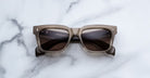 Jacques Marie Mage Torino sunglasses by Jacques Marie Mage, featuring square gray frames and dark lenses, are premium Japanese eyewear. Displayed on a white marble surface, they are photographed from above.