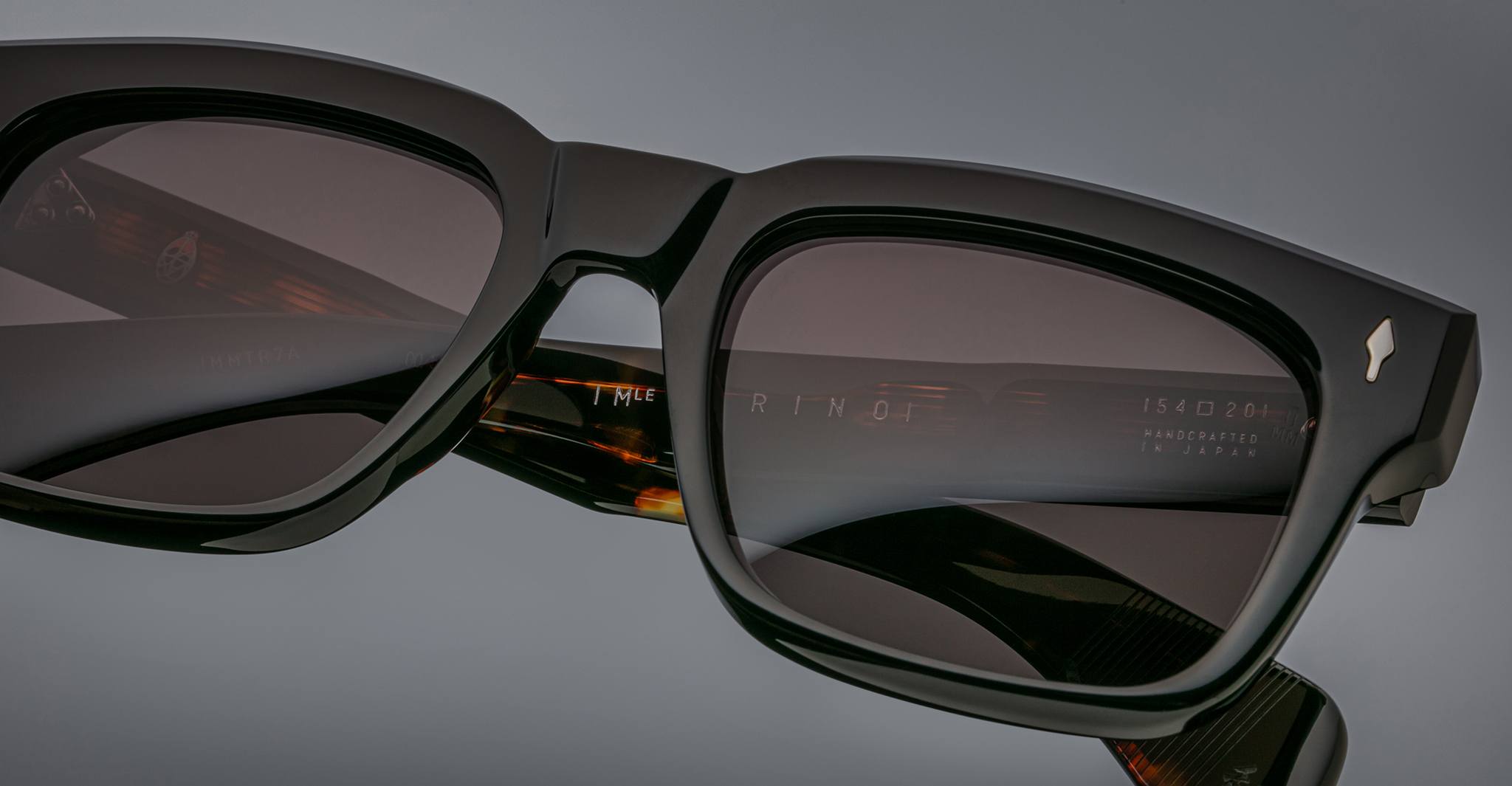 Close-up of Jacques Marie Mage Torino bold rectangular black acetate frames, featuring dark lenses and “Handcrafted in Japan” on the inner arm, highlighting the brand's exquisite craftsmanship.