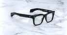 A pair of Jacques Marie Mage Torino black rectangular eyeglass frames by Jacques Marie Mage rests on a white marble surface.